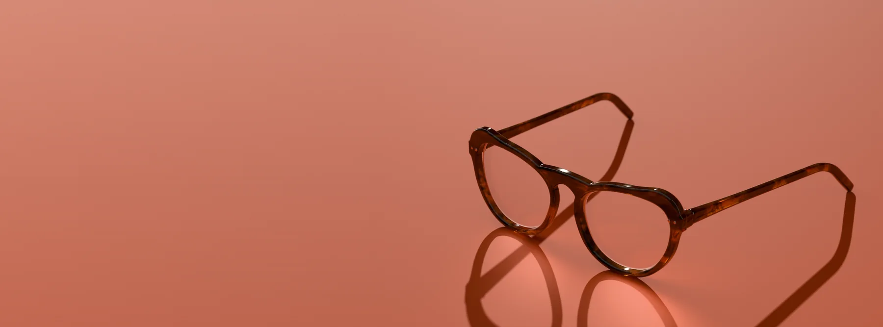 Alba cat-eye glasses in Amber tortoise, in low sun on a terracotta ground