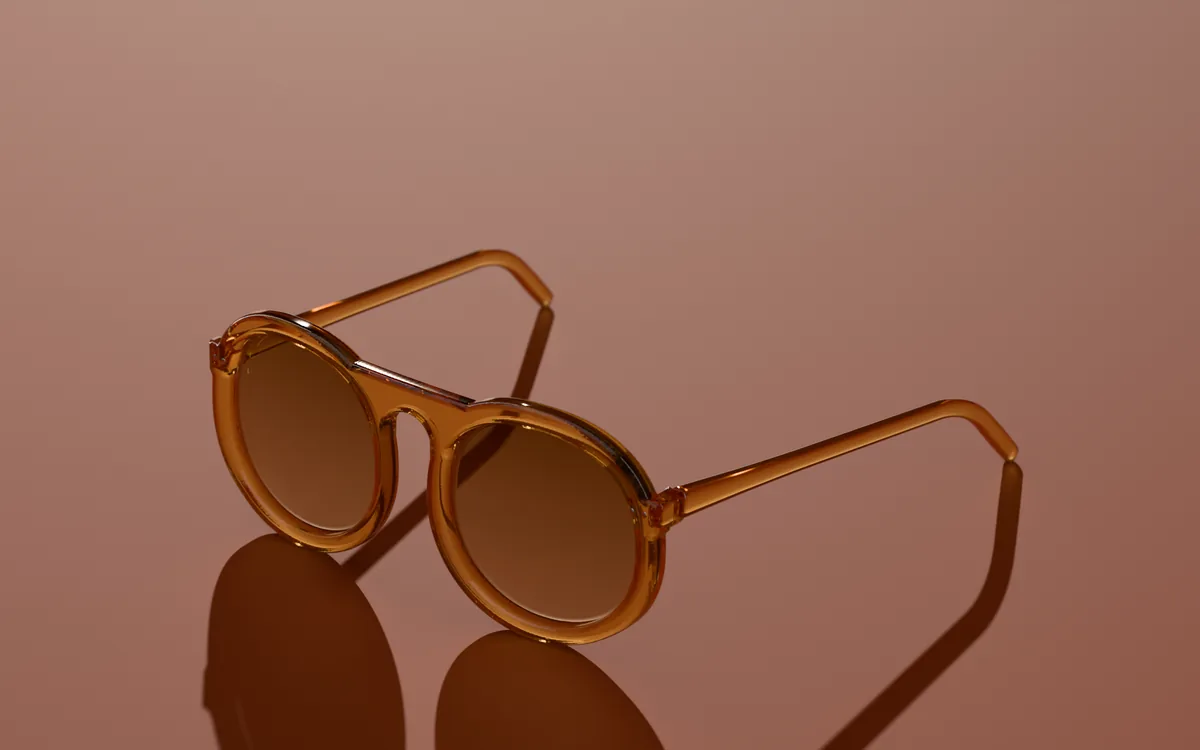 Noor round sunglasses in Honey amber, in low sun on a warm ground